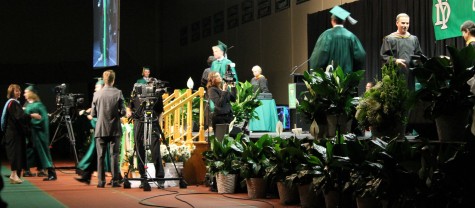 Graduates walk onto the stage to shake hands and receive diplomas .  