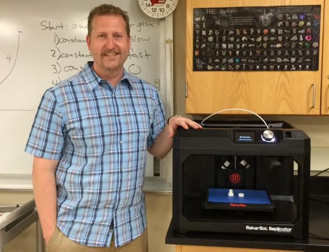 Mr.Drach next to the MakerBot Replicator 3D printer in his classroom, A360.
