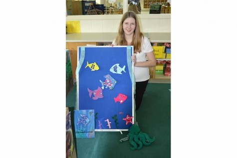 Emma Vezmar poses next to her Children’s Literature presentation inspired by The Rainbow Fish, a classic children’s book. 