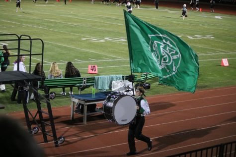 Showing marching band pride, junior Andrew Hilgendorf runs down the track with the marching band flag stuck in his bass drum harness.