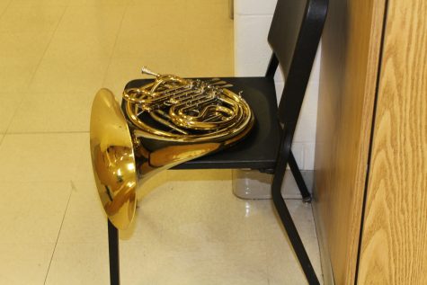 A french horn sulks on a chair in isolation. 