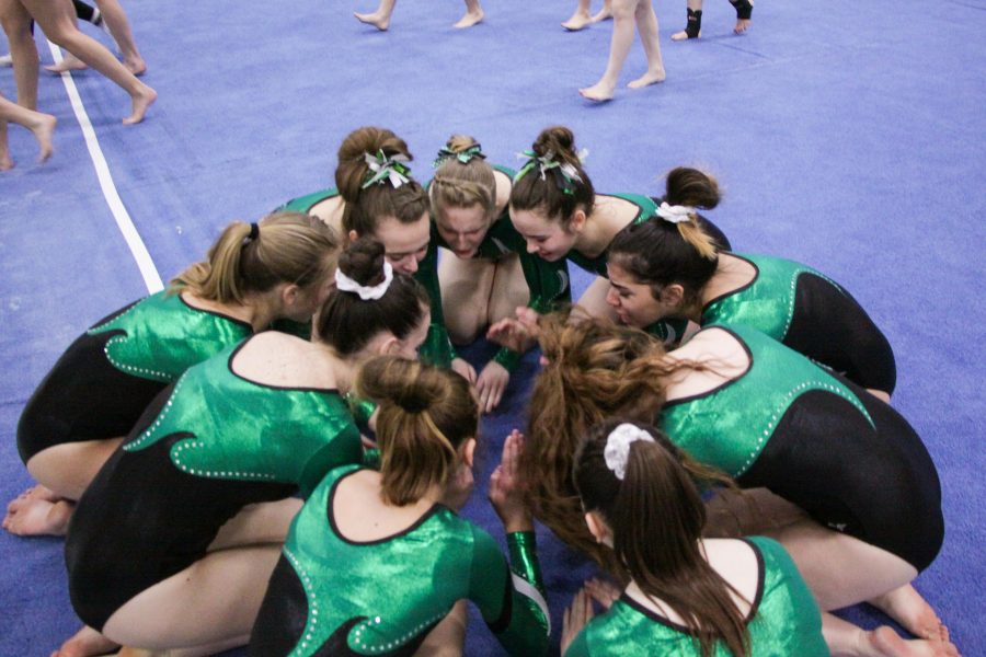 The girls gymnastics team yells out their pre-meet chant before they begin to perform. 