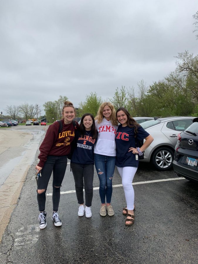 Seniors Lily Kraus, Elysia Woodward, Ellie Davis, and Chloe Gomez pose in their college gear by their parking spots.