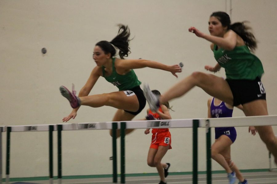 Junior Tessa Spedale and senior Emma Lutz leap over the hurdle as they compete in the varsity 55m hurdles.