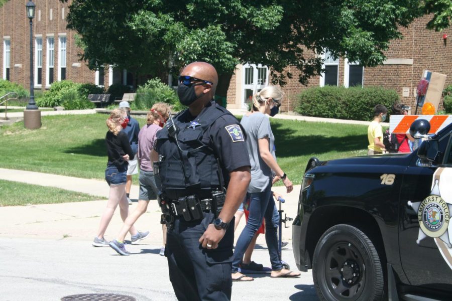 An Elmhurst Police officer stands in front of his vehicle to monitor crowd behavior during the Elmhurst March for Equality protest to ensure peaceful actions. Police cars were parked at all corners of the route, blockading cars from entering. June 13, 2020.