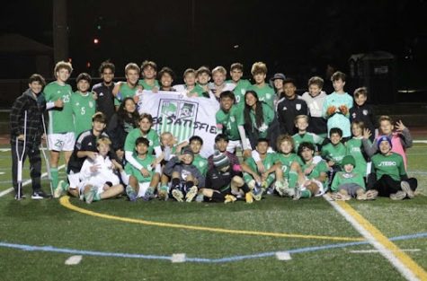 The York soccer team and managers pose in front of a banner displaying this years team motto, “Never Satisfied.” 

